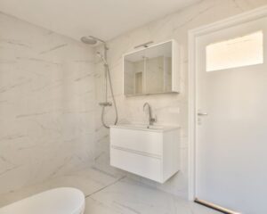 A new white bathroom featuring a toilet and shower with tiled walls and floors.