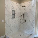 A marble shower with a shower head in an elegant bathroom design.