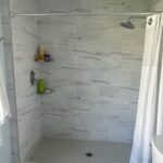A white tiled bathroom with a toilet and shower.