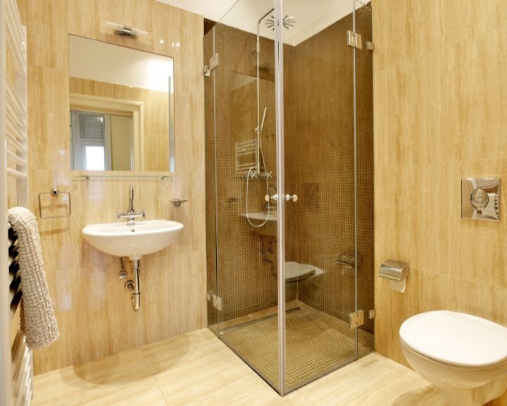 A glass shower stall, sink and toilet in a city bathroom.